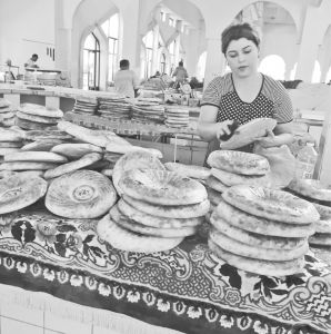 图9 在布哈拉的集市上，一位面包商人正在擦拭刚刚从乌兹别克式馕坑烤好的新鲜扁面包，2017年