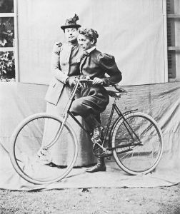 约1895年，玛丽亚·“维奥莉特”·沃德（Maria “Violet” Ward）正扶着黛西·艾略特（Daisy Elliott）骑自行车。